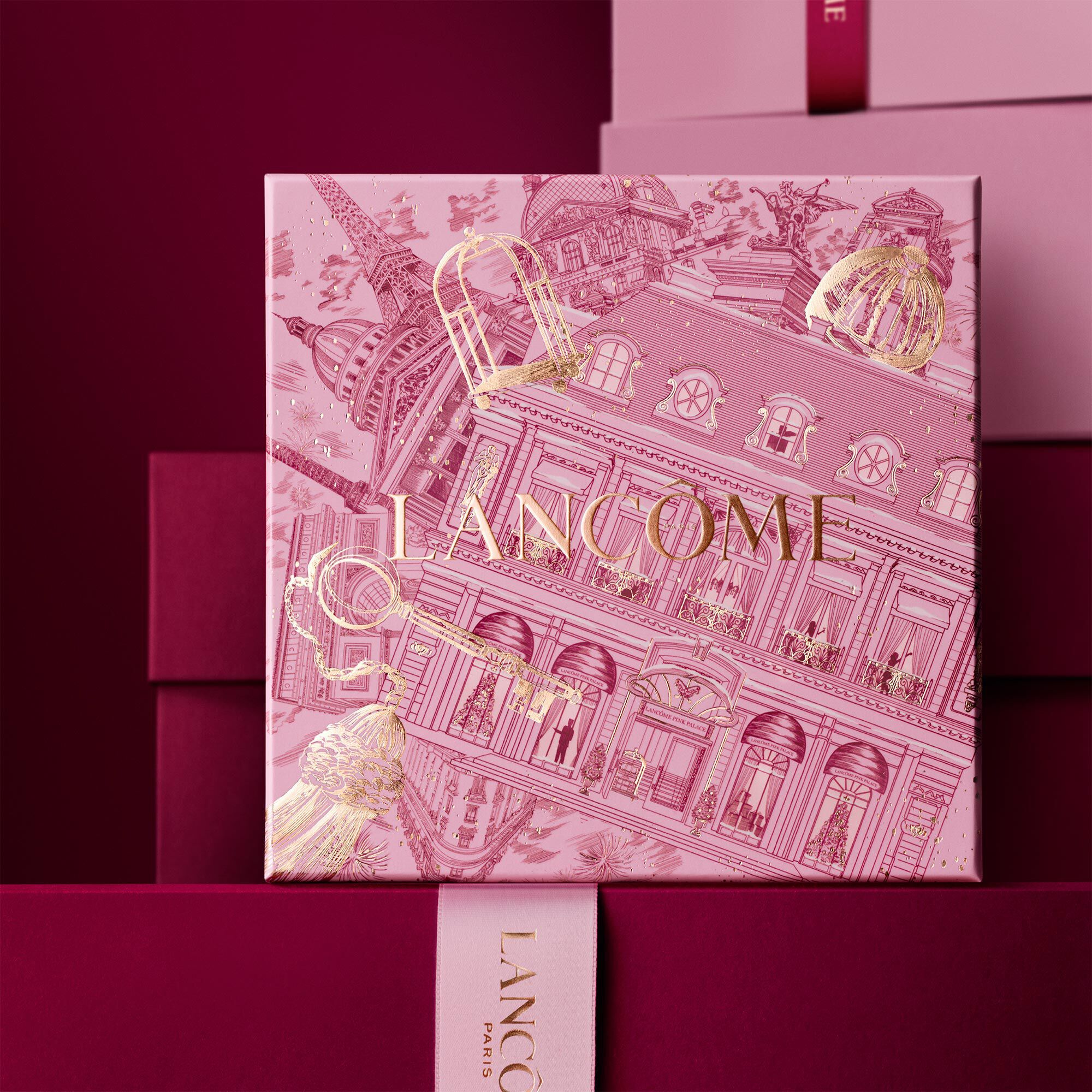 Bild einer rosafarbenen Lancome-Weihnachtsgeschenkbox vor einem Haufen rosa und dunkelroter Geschenkboxen, die vor einem dunkelroten Hintergrund stehen.