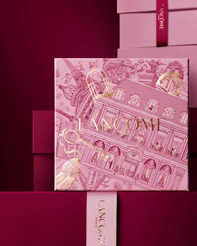 Ein eleganter Stapel aus rosa und tief burgunderroten Lancome-Geschenkboxen, in dessen Mitte eine Box mit goldenen Illustrationen der Pariser Architektur zu sehen ist.