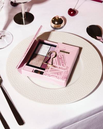 Eine rosafarbene Lancome-Lidschattenpalette mit goldenem Schlusselloch-Motiv, elegant prasentiert auf einem weißen Essteller.