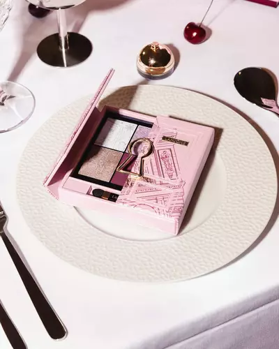 Eine rosafarbene Lancome-Lidschattenpalette mit goldenem Schlusselloch-Motiv, elegant prasentiert auf einem weißen Essteller.