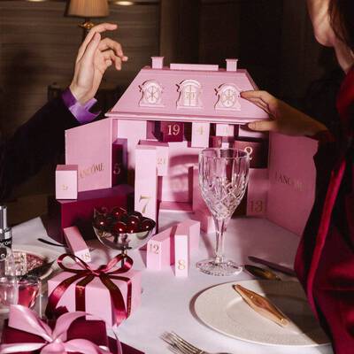 Hande interagieren mit einem rosafarbenen Adventskalender von Lancome auf einem festlichen gedeckten Esstisch.