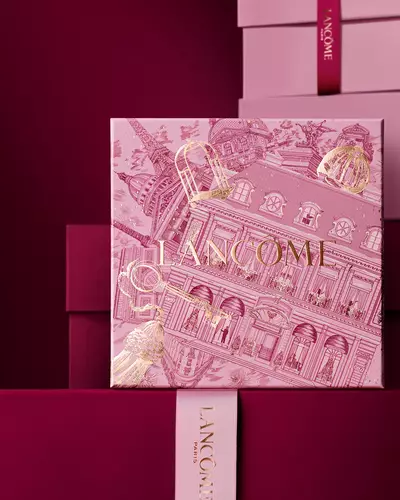 Ein eleganter Stapel aus rosa und tief burgunderroten Lancome-Geschenkboxen, in dessen Mitte eine Box mit goldenen Illustrationen der Pariser Architektur zu sehen ist.
