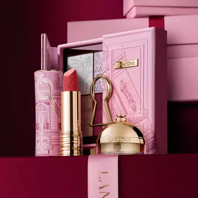 Ein sorgfaltig zusammengestelltes Weihnachtsgeschenkset von Lancome mit einem Lippenstift, einer Lidschattenpalette und einem goldenen Highlighter, prasentiert vor einem dekorativen rosa Etui.