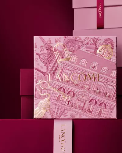 Ein eleganter Stapel aus rosa und tief burgunderroten Lancome-Geschenkboxen, in dessen Mitte eine Box mit goldenen Illustrationen der Pariser Architektur zu sehen ist.