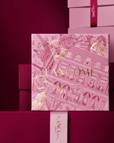 Bild einer pinken Lancome-Weihnachtsgeschenkbox vor einem Haufen rosa und dunkelroter Geschenkboxen, die vor einem dunkelroten Hintergrund stehen.