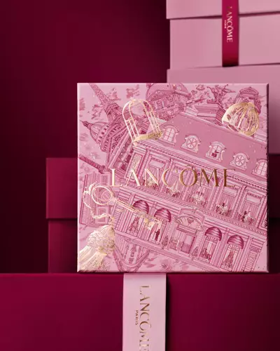 Bild einer pinken Lancome-Weihnachtsgeschenkbox vor einem Haufen rosa und dunkelroter Geschenkboxen, die vor einem dunkelroten Hintergrund stehen.