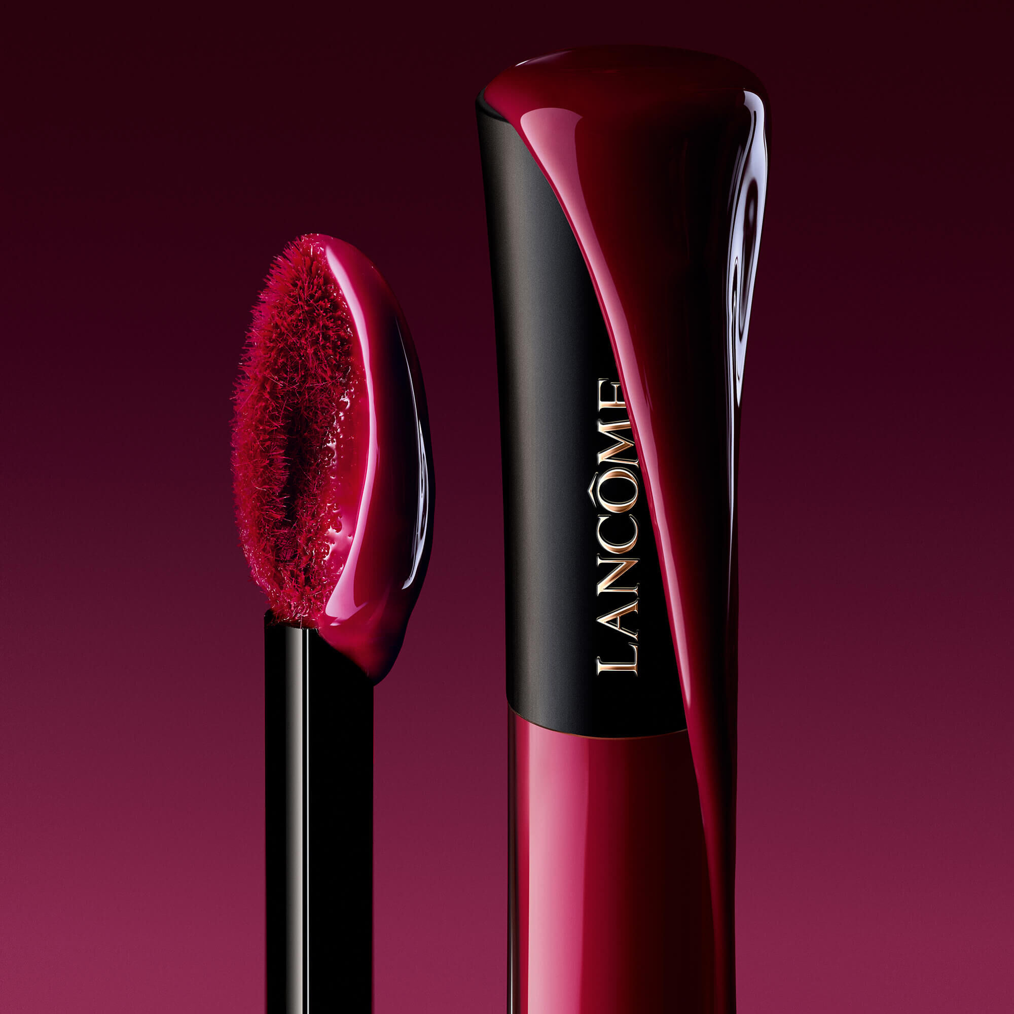 Eine kunstlerische Nahaufnahme einer Lancome L'Absolu Rouge Glaze Tintation-Tube mit reichem, glanzendem Pigment, das neben einem weichen, gesattigten Applikator-Wand heruntertropft.