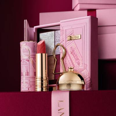 Ein sorgfaltig zusammengestelltes Weihnachtsgeschenkset von Lancome mit einem Lippenstift, einer Lidschattenpalette und einem goldenen Highlighter, prasentiert vor einem dekorativen rosa Etui.