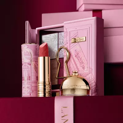 Ein sorgfaltig zusammengestelltes Weihnachtsgeschenkset von Lancome mit einem Lippenstift, einer Lidschattenpalette und einem goldenen Highlighter, prasentiert vor einem dekorativen rosa Etui.