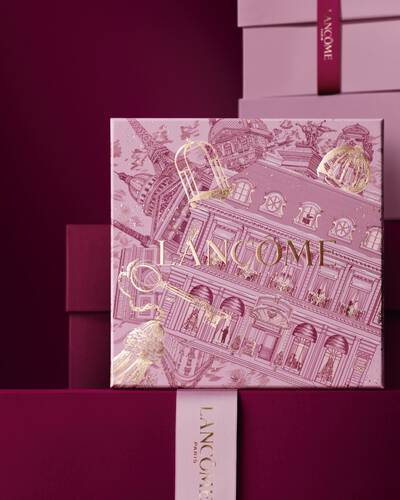 Bild einer rosafarbenen Lancome-Weihnachtsgeschenkbox vor einem Haufen rosa und dunkelroter Geschenkboxen, die vor einem dunkelroten Hintergrund stehen.