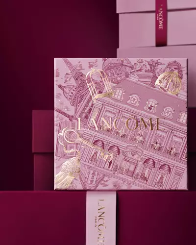 Bild einer rosafarbenen Lancome-Weihnachtsgeschenkbox vor einem Haufen rosa und dunkelroter Geschenkboxen, die vor einem dunkelroten Hintergrund stehen.