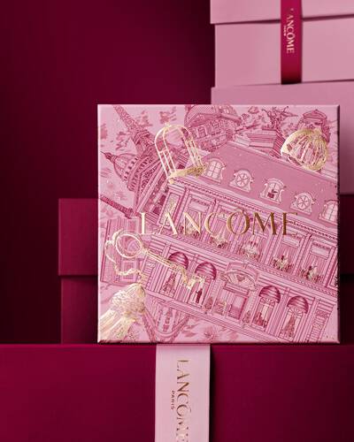 Bild einer rosafarbenen Lancome-Weihnachtsgeschenkbox vor einem Haufen rosa und dunkelroter Geschenkboxen, die vor einem dunkelroten Hintergrund stehen.