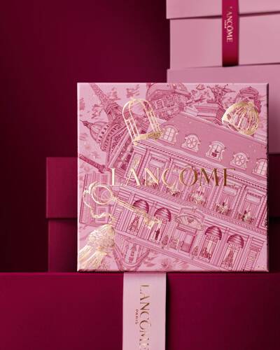 Ein eleganter Stapel aus rosa und tief burgunderroten Lancome-Geschenkboxen, in dessen Mitte eine Box mit goldenen Illustrationen der Pariser Architektur zu sehen ist.