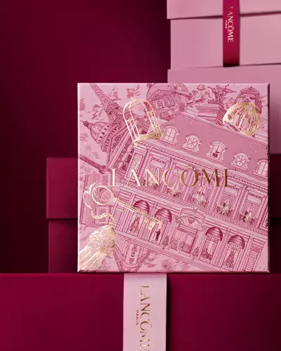 Bild einer rosafarbenen Lancome-Weihnachtsgeschenkbox vor einem Haufen rosa und dunkelroter Geschenkboxen, die vor einem dunkelroten Hintergrund stehen.