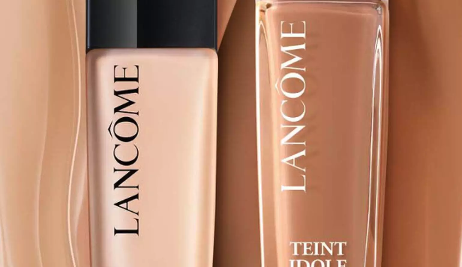 Zwei Flaschen von Lancome Teint Idole Ultra Wear Foundation, eine mit schwarzem Deckel und eine mit weißem Deckel, auf einem beigen Hintergrund.