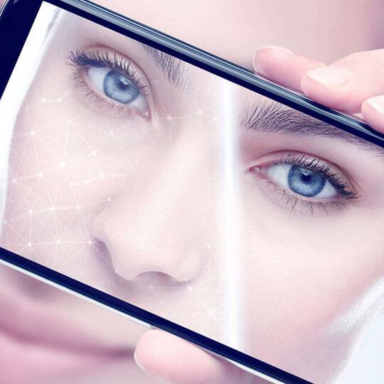 Dekoratives Bild: Nahaufnahme des Gesichts einer Frau, die ein Handy zur Hautanalyse uber ihr Gesicht halt