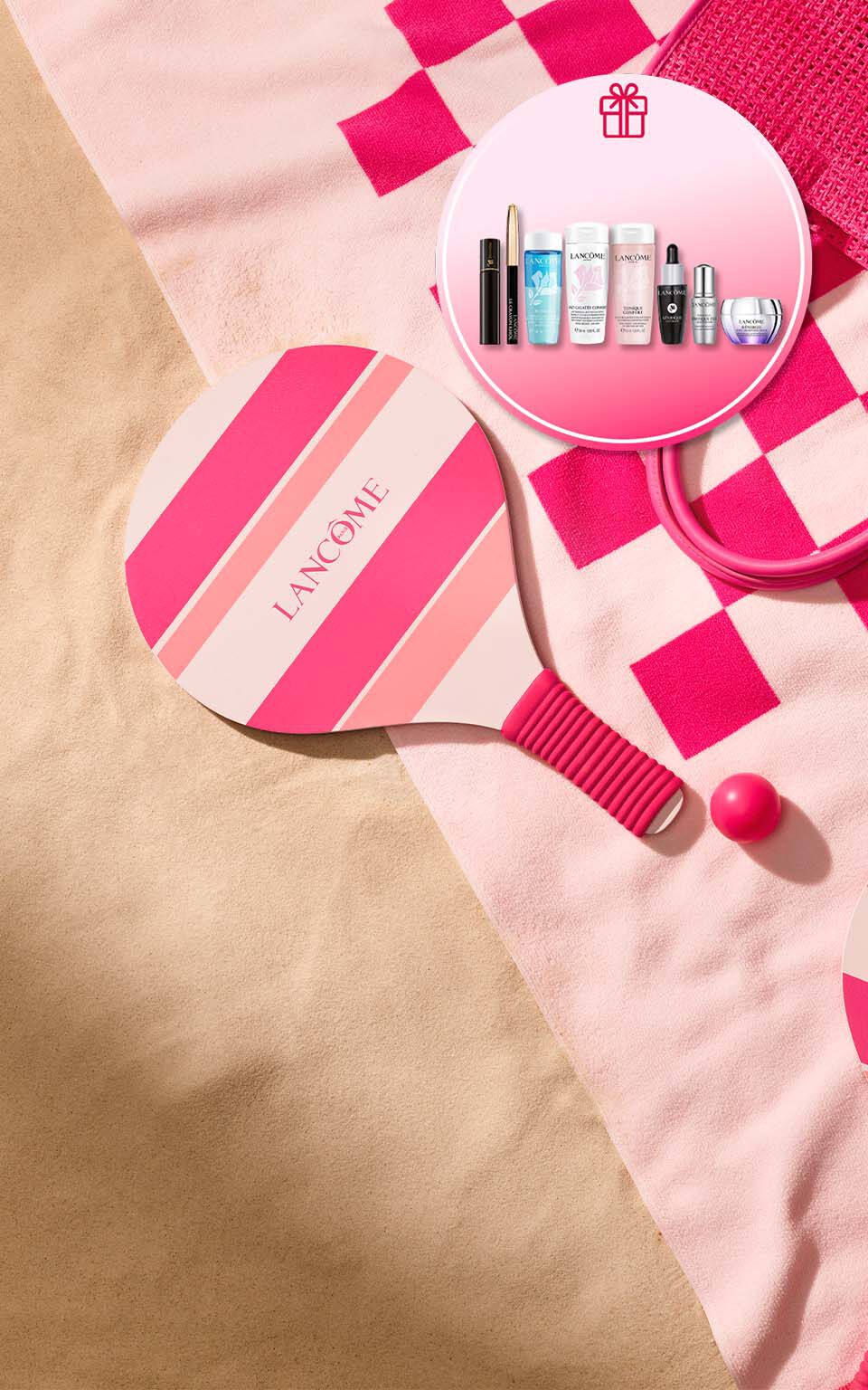 Lancome Sommer-Promotion-Banner am Strand mit einem rosa-pink gestreiften Strand-Tennisschlager und passendem Ball auf einem Handtuch im Sand. Ein runder Einleger oben rechts mit einem Geschenk-Symbol zeigt das exklusive Gratis-Geschenkset mit Lancome-Miniaturen, darunter Reinigungsprodukte wie Bi-Facil und Tonique Confort, ein Augenkajal, Mascara sowie Advanced Genifique und Renergie Pflegeprodukte.