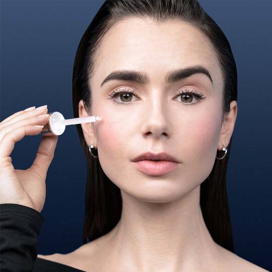Dekoratives Bild: Nahaufnahme des Gesichts einer Frau, die mit einem Dropper Serum auf ihre Wange auftragt