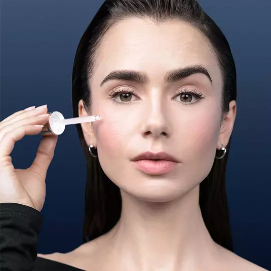 Dekoratives Bild: Nahaufnahme des Gesichts einer Frau, die mit einem Dropper Serum auf ihre Wange auftragt