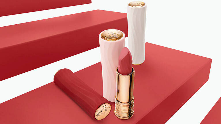 Zwei Lippenstifte auf roten Treppenstufen, einer geoffnet mit zartem Rosa und der andere in einer eleganten Hulle.