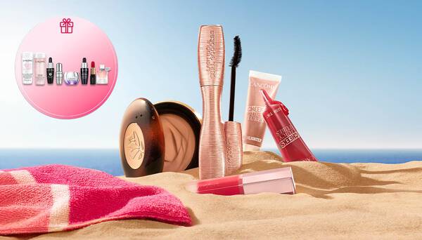 Lancome Sommer-Make-up im Sand mit einem runden Geschenk-Symbol auf der linken Seite und viel freiem Platz vor blauem Himmel und Meer rechts