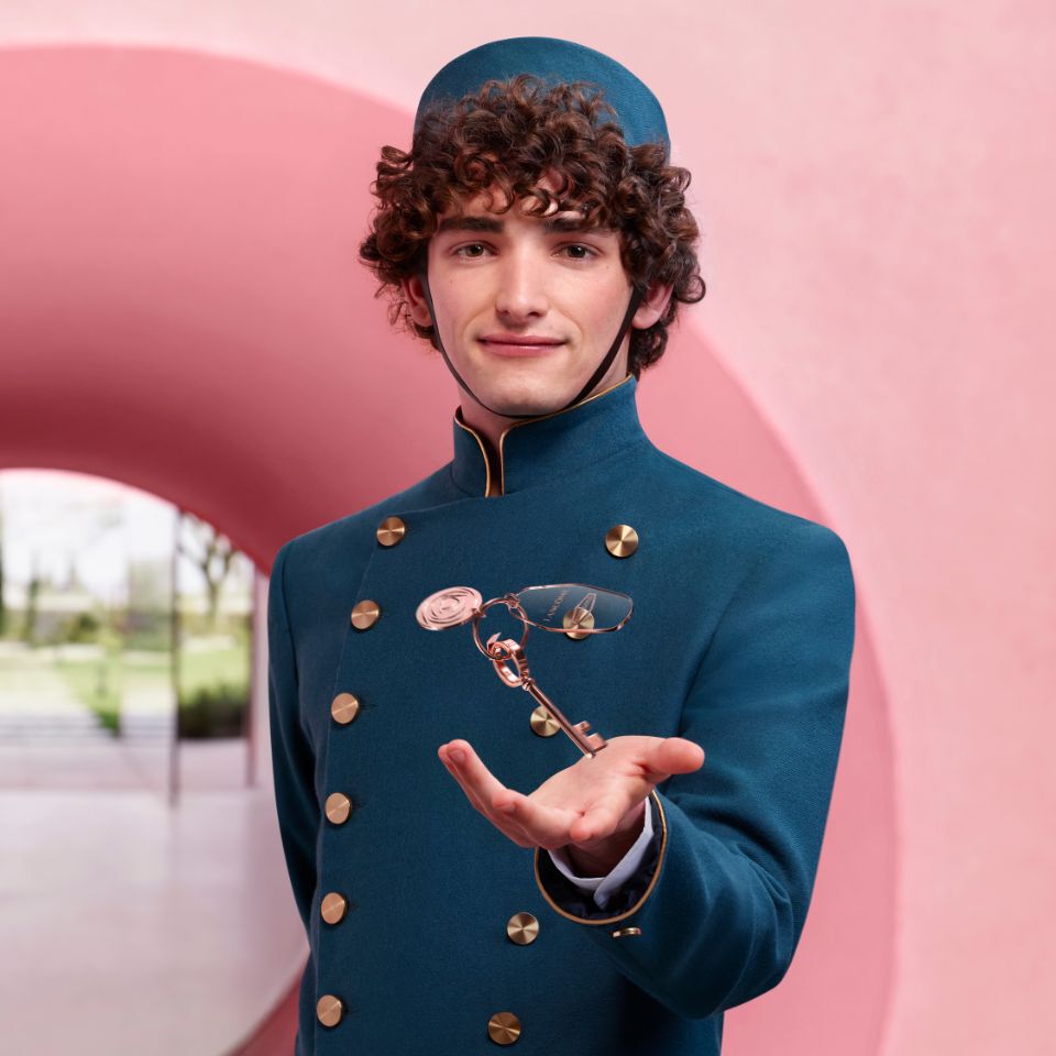 Eine Frau halt mehrere Lancome-Pakete in den Handen und lachelt. Im Hintergrund ist eine rosa Wellenform zu sehen. Text: "Werde Teil der Lancommunity".