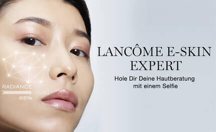 Eine Frau mit glatter Haut betrachtet sich im Spiegel, wahrend sie auf ein digitales Hautanalyse-Tool auf ihrem Gesicht schaut. Der Text sagt: "LANCOME E-SKIN EXPERT - Hole Dir Deine Hautberatung mit einem Selfie."
