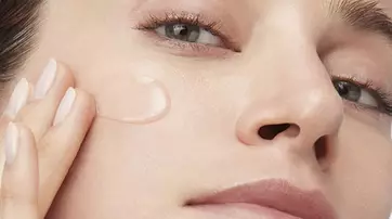 Eine Frau tragt ein transparentes Gel auf ihr Gesicht auf und schaut dabei in die Kamera.