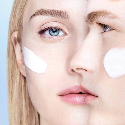 Ein close-up von zwei Gesichtern, die eine Creme auf die Wangen auftragen, vor einem blauen Hintergrund.