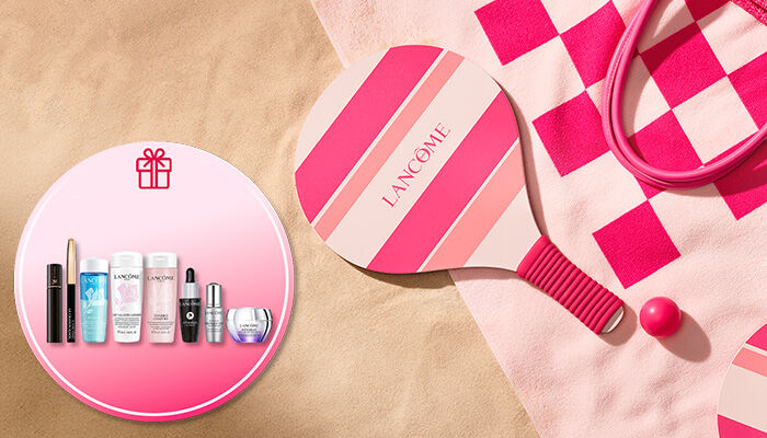 Lancome Sommer-Promotion-Banner am Strand mit einem rosa-pink gestreiften Strand-Tennisschlager und passendem Ball auf einem Handtuch im Sand. Ein runder Einleger oben rechts mit einem Geschenk-Symbol zeigt das exklusive Gratis-Geschenkset mit Lancome-Miniaturen, darunter Reinigungsprodukte wie Bi-Facil und Tonique Confort, ein Augenkajal, Mascara sowie Advanced Genifique und Renergie Pflegeprodukte.