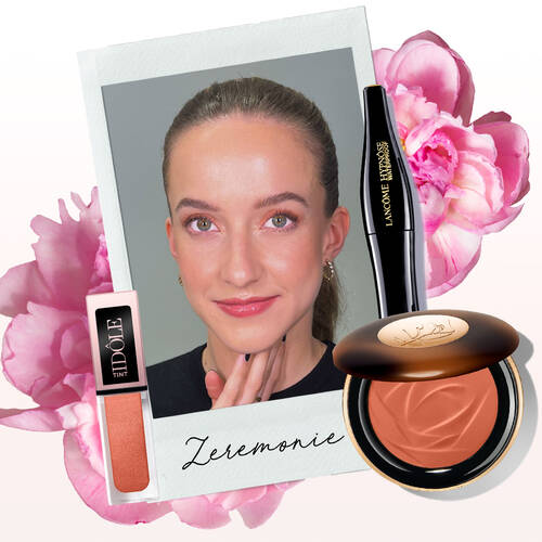Eine Frau mit dezentem Make-up, die einen handgestutzten Gesichtsausdruck macht. Neben ihr sind ein Lippen-Tint von Idole und ein Bronzer von Lancome abgebildet. Im Hintergrund sind Rosa-Bluten zu sehen und das Wort "Zeremonie" steht auf einer Polaroid-ahnlichen Karte.