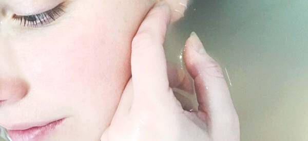 Frau liegt im Wasser und streicht mit ihrem Zeigefinger sanft uber ihr Gesicht