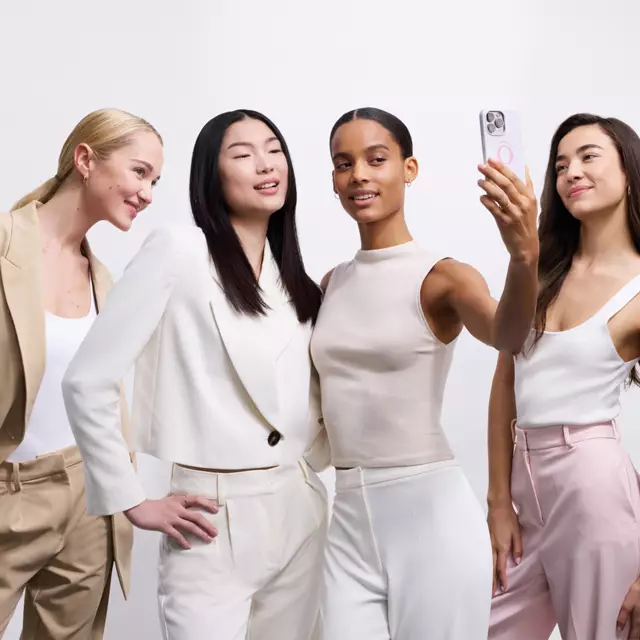 Vier Frauen in modischer Kleidung posieren fur ein Selfie vor einem neutralen Hintergrund.
