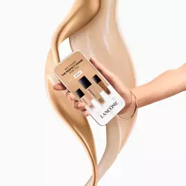 Hand halt Smartphone mit Lancome Foundation-Farbabgleich vor wirbelndem Foundation-Hintergrund.