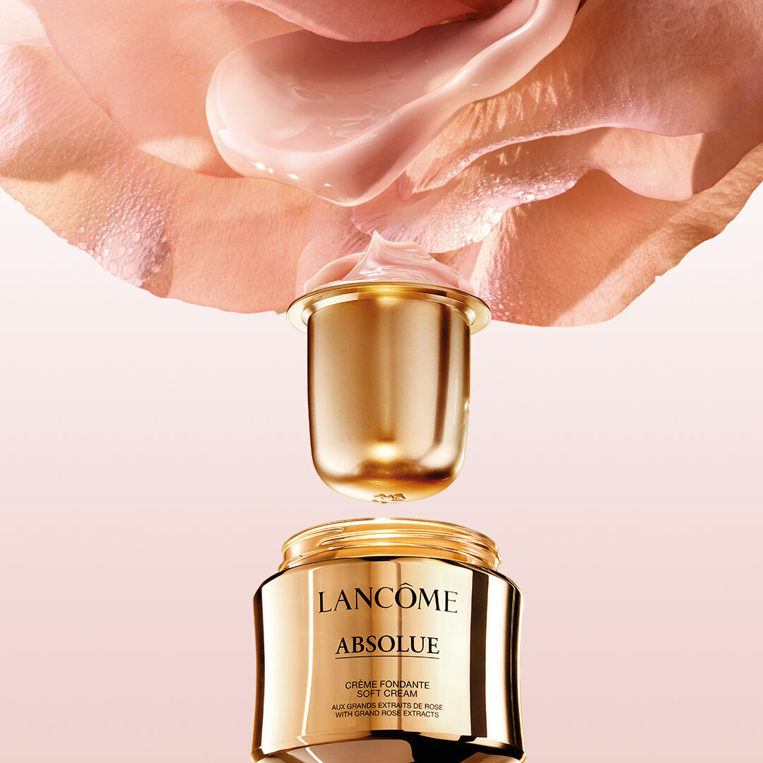 Eine Nahaufnahme eines goldenen Cremetopfs von Lancome Absolue mit einem Rosenausschnitt im Hintergrund und einer sanften Creme, die aus dem Deckel tropft.