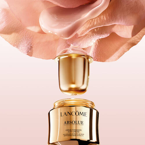 Eine Nahaufnahme eines goldenen Cremetopfs von Lancome Absolue mit einem Rosenausschnitt im Hintergrund und einer sanften Creme, die aus dem Deckel tropft.