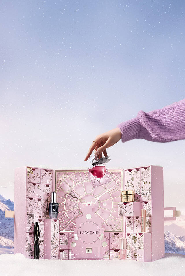 Ein dekorativer Adventskalender von Lancome, der verschiedene Kosmetikprodukte enthalt, wird geoffnet. Glitzernde Sterne sind im Hintergrund zu sehen.