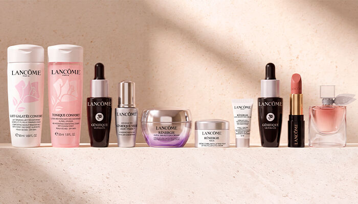 Eine Auswahl an Lancome-Beauty- und Pflegeprodukten, darunter Lait Galatee Confort, Tonique Confort, Genifique Ultime, Renergie-Cremes, ein Lippenstift und ein La Vie Est Belle Parfum, prasentiert auf einer hellen, strukturierten Oberflache.