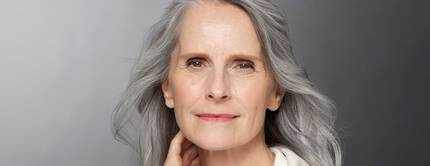 Eine altere Frau mit langen grauen Haaren und einer sanften Ausstrahlung, die direkt in die Kamera schaut.