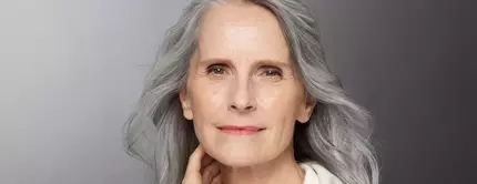 Eine altere Frau mit langen grauen Haaren und einer sanften Ausstrahlung, die direkt in die Kamera schaut.