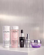 Hande halten Lancome Genifique Seren neben einem Geschenk-Symbol mit einem Aktions-Set auf der rechten Seite.