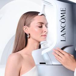 Amanda Seyfried mit geschlossenen Augen bei einer professionellen Hautanalyse mit dem Lancome Skin Screen Gerat vor einem geschwungenen, weißen abstrakten Hintergrund.