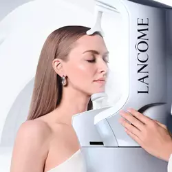 Amanda Seyfried mit geschlossenen Augen bei einer professionellen Hautanalyse mit dem Lancome Skin Screen Gerat vor einem geschwungenen, weißen abstrakten Hintergrund.