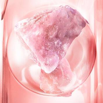 Ein glitzernder rosa Kristall, der in einem durchsichtigen Behalter auf einem glanzenden Untergrund prasentiert wird.