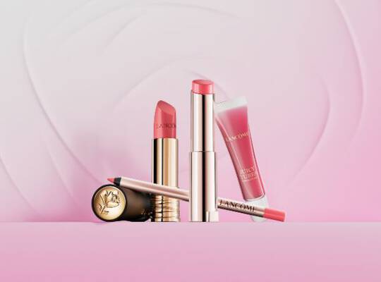 Eine Kollektion von Lancome Make-up-Produkten, darunter eine Lidschattenpalette, ein Kompaktpuder und ein roter Lippenstift, alle in eleganter rosa-goldener Verpackung.