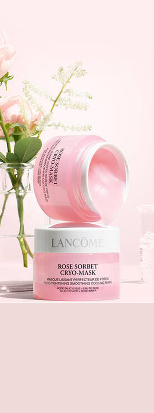 Eine rosa Hautmaske von Lancome mit einem Glas Wasser und Rosen in einer Vase im Hintergrund.