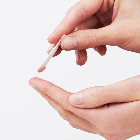 Eine Hand halt einen Applikator, der gerade eine kleine Menge einer Creme oder eines Produkts auf die andere Hand auftragt.