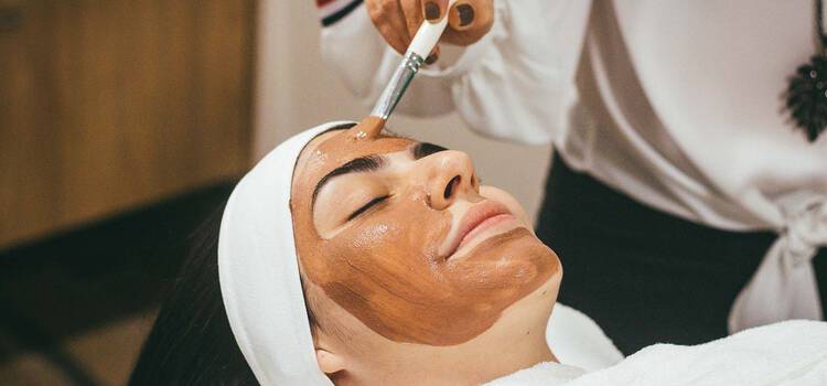 Frau mit geschlossenen Augen liegt und bekommt eine Anti-Aging Behandlung mit Gesichtsmaske