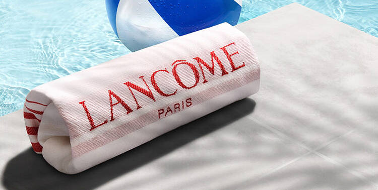 Ein Badetuch von Lancome und ein Ball an einem Pool im Sommer.