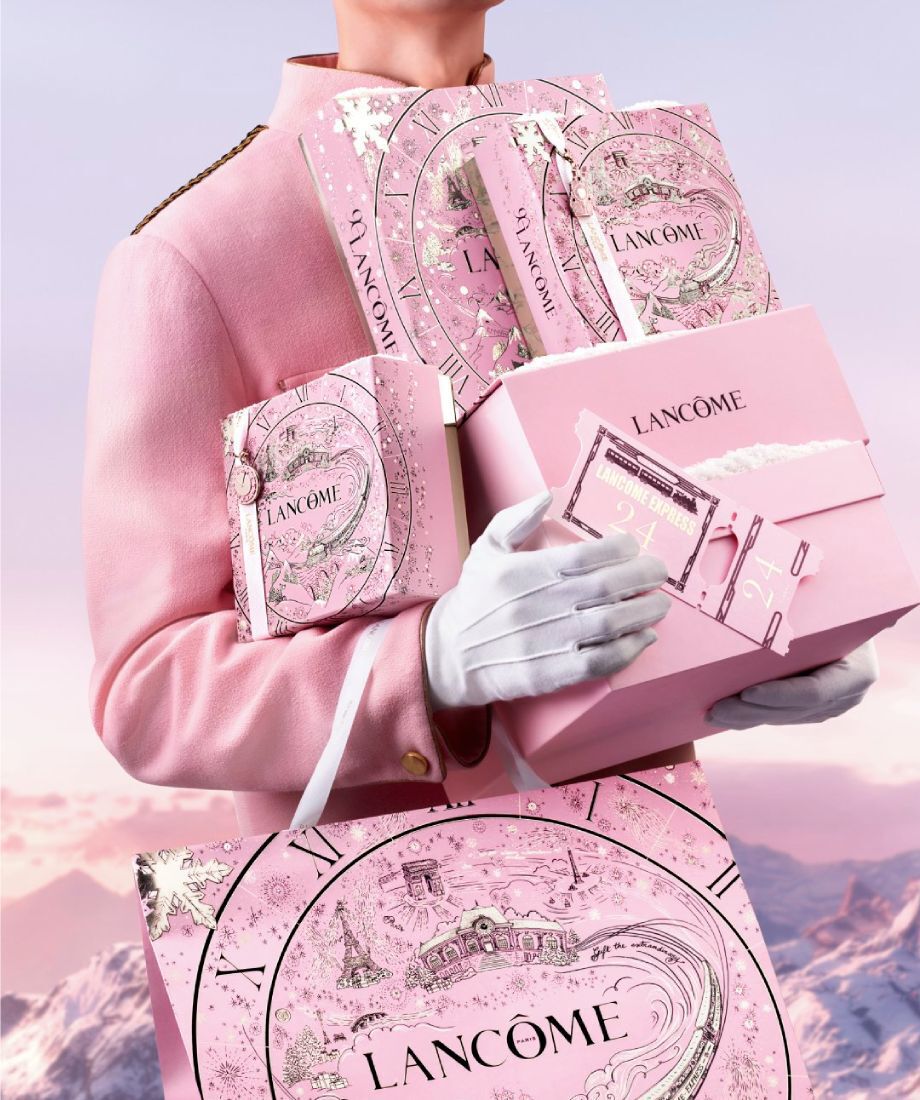 Eine Person tragt mehrere elegante Geschenkboxen von Lancome, die in dunklen Farben mit goldenen Akzenten gestaltet sind.